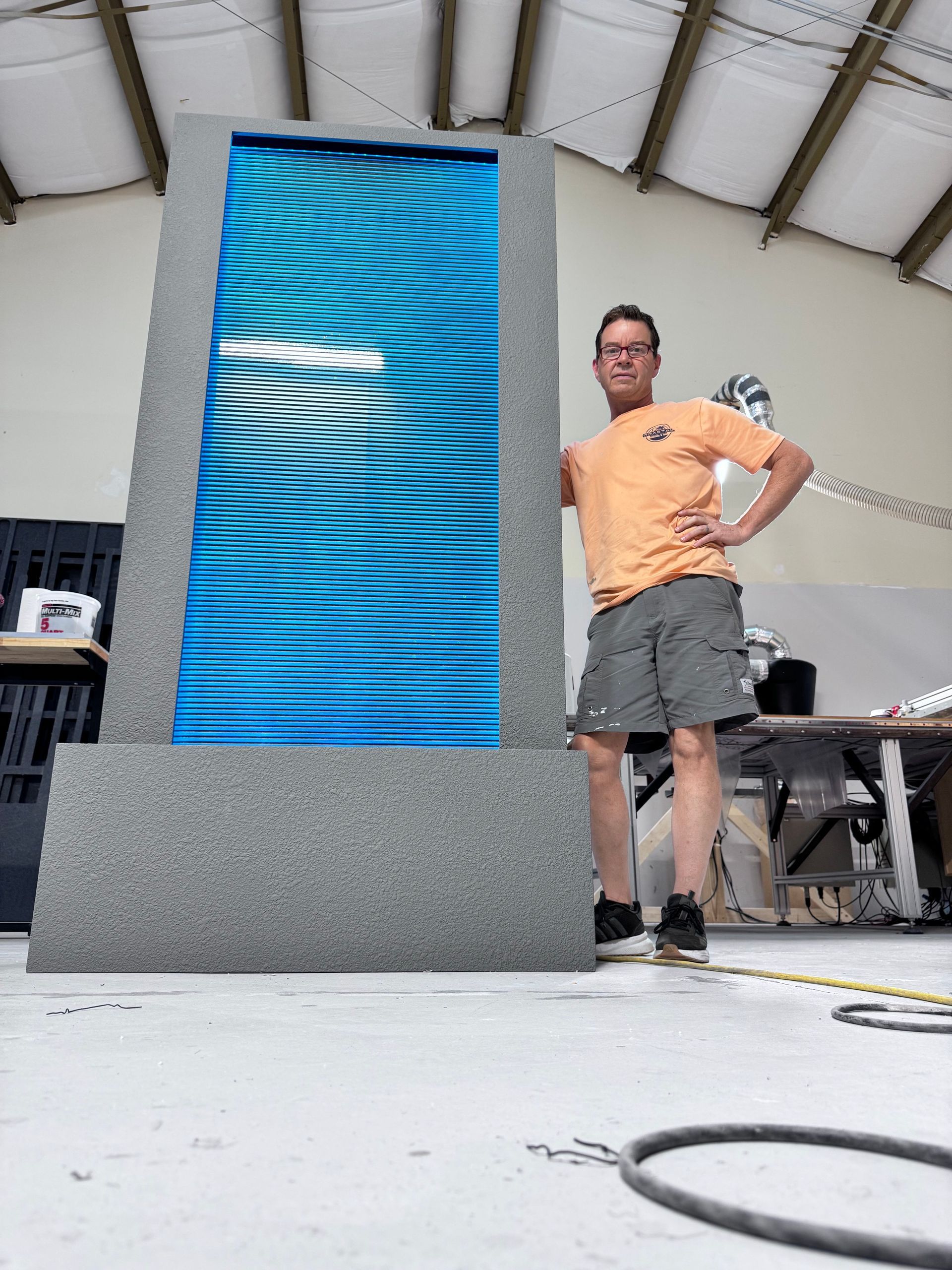 Man standing next to a large water feature with blue wavy patterns, in a workshop setting