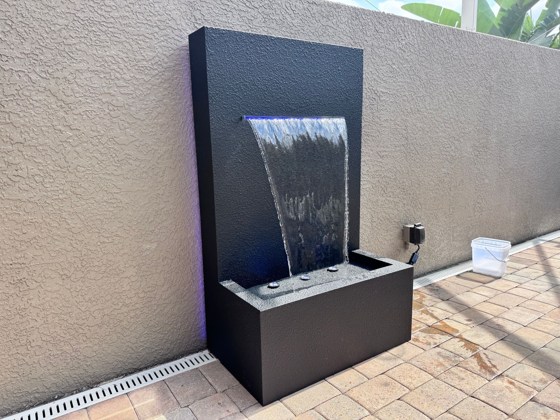 Water fountain with black stone finish against a beige stucco wall, water cascading