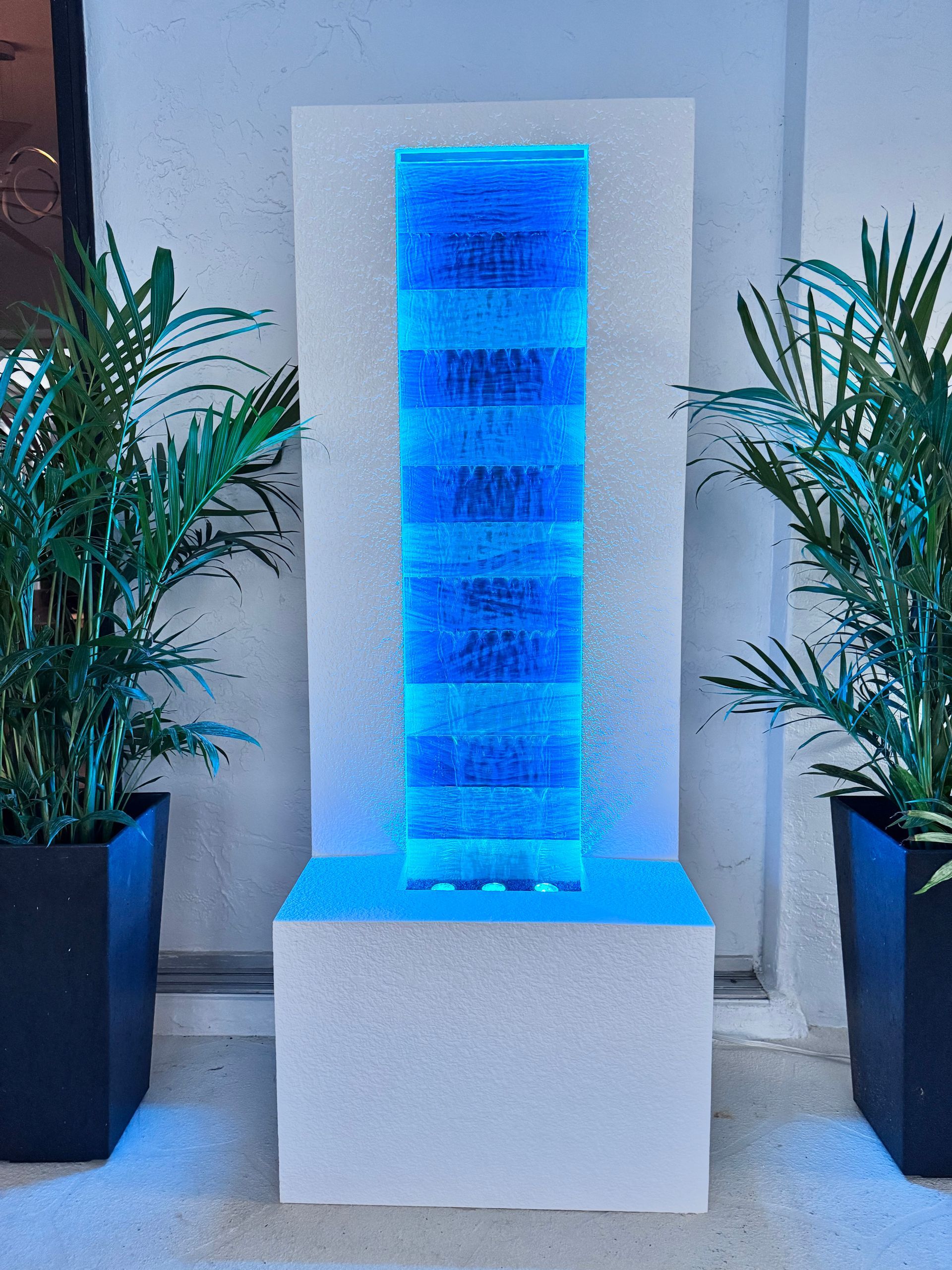 Blue illuminated water fountain with plants on either side