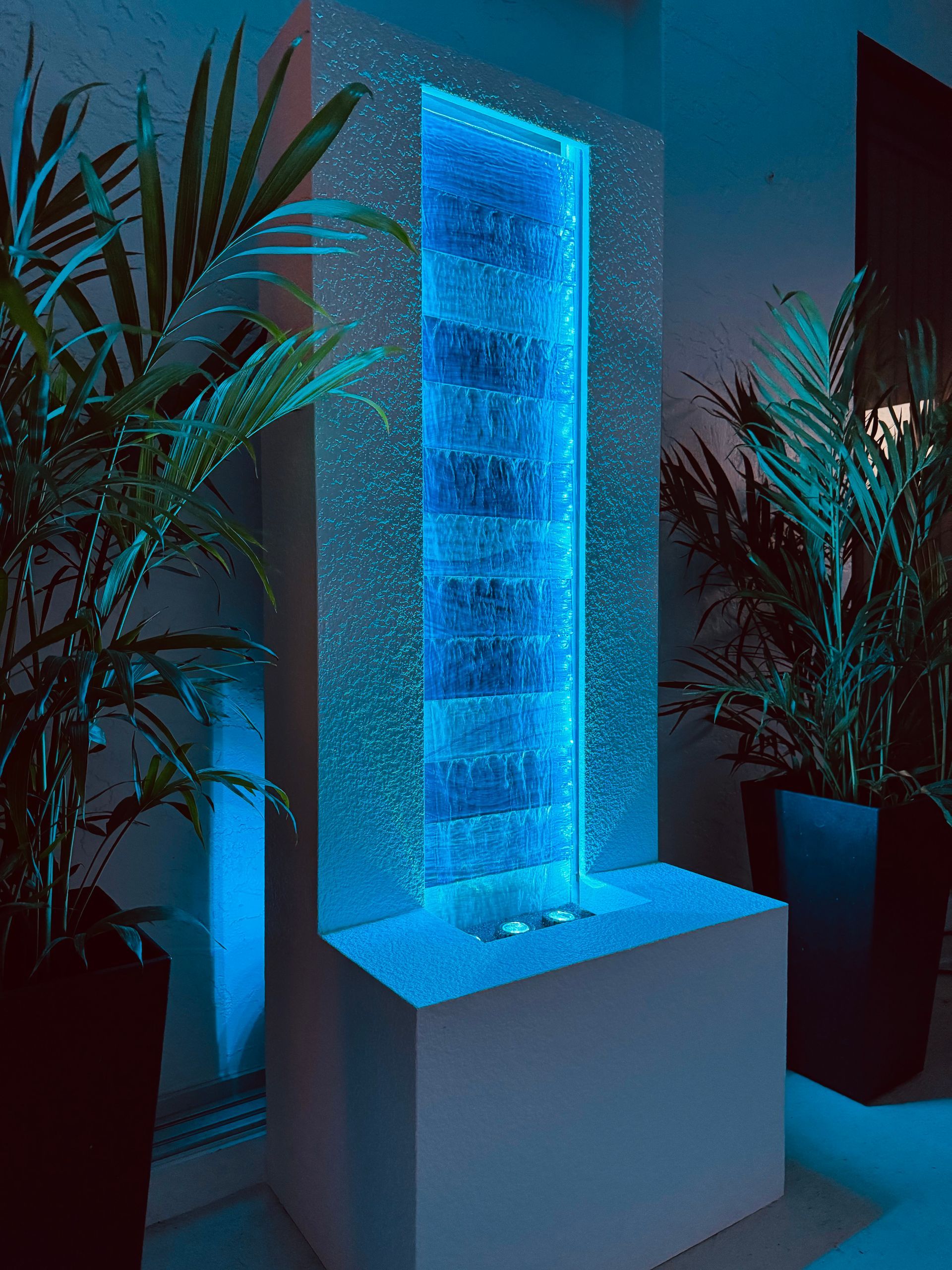 Blue illuminated bubble fountain with plants on either side