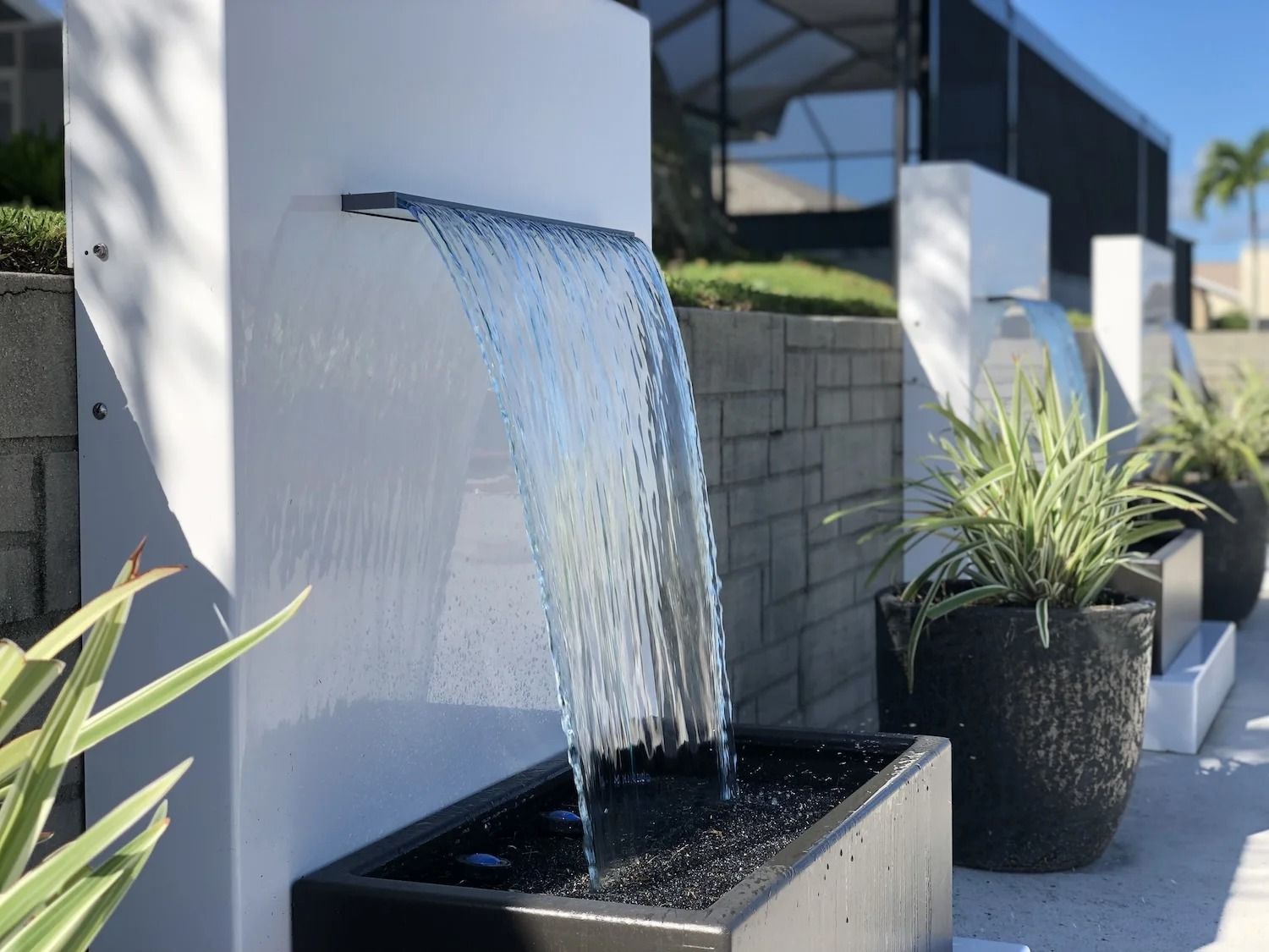 Waterfall fountain feature with water flowing into a rectangular basin, next to potted plants