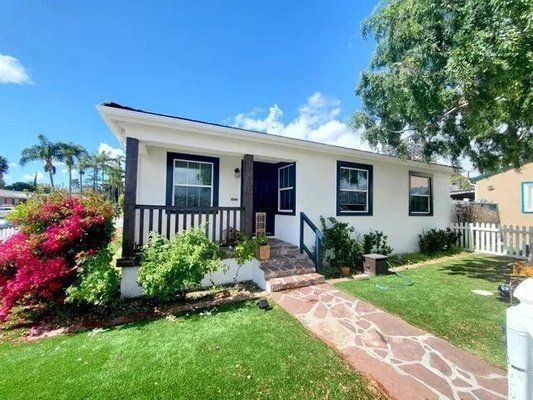 Man painting exterior wall with white paint near a window.