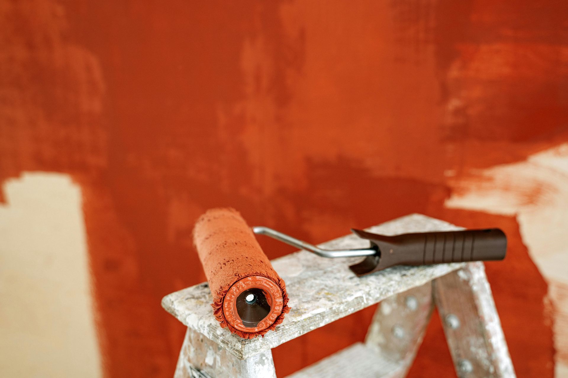 Person painting a wall with a paint roller in a room. Beige walls, beige paint swatch.
