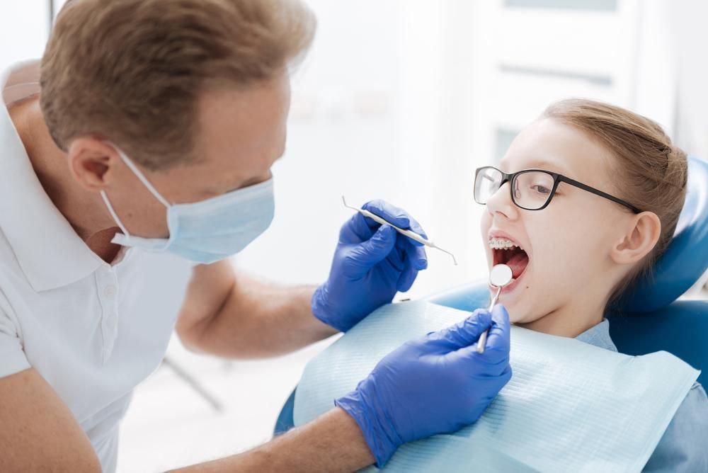 A Young Girl Is Sitting in A Dental Chair While a Dentist Examines Her Teeth — Steve King Dental Group in Manunda, QLD