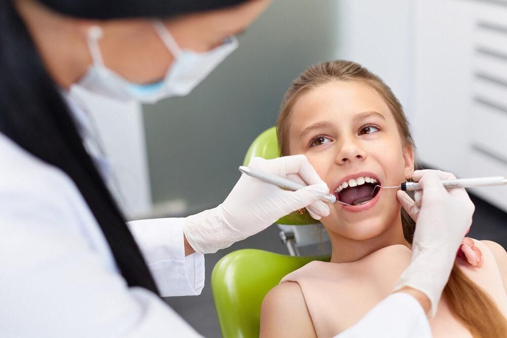 A Young Girl Is Sitting in A Dental Chair Getting Her Teeth Examined by A Dentist — Steve King Dental Group in Mossman, QLD