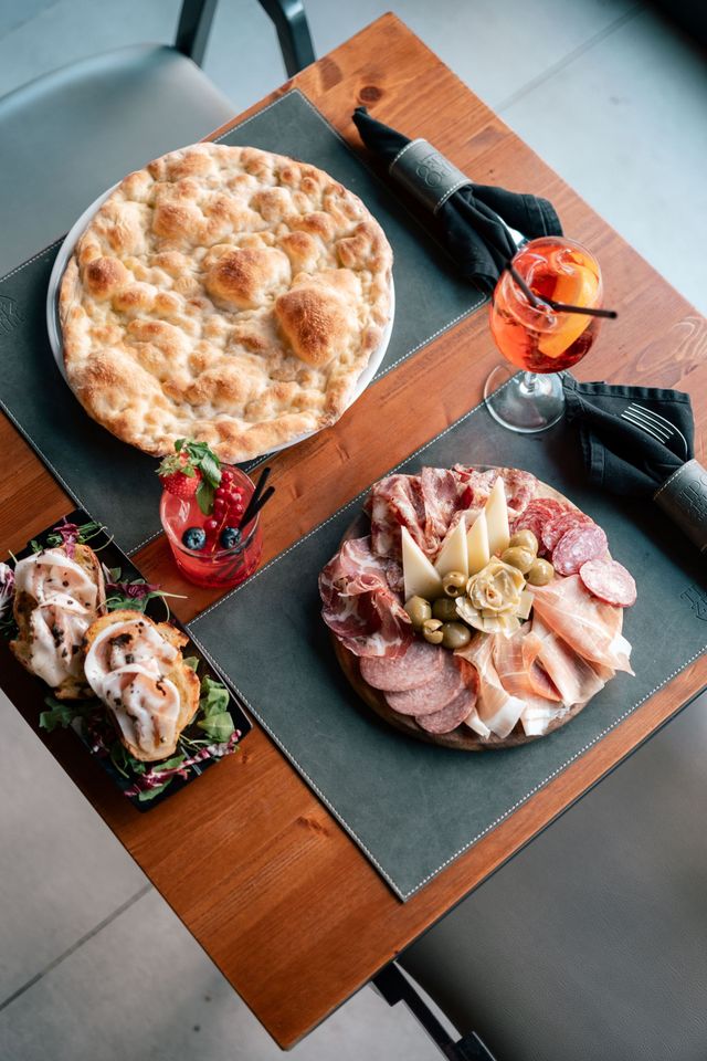 Pizze assortite e piatti unici su un tavolo di legno con bevande e posate.