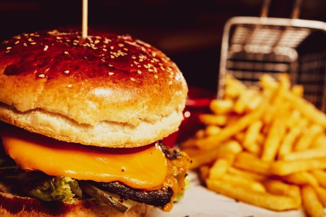 Primo piano di un cheeseburger con patatine fritte su un vassoio, guarnito con semi di sesamo e uno stuzzicadenti.