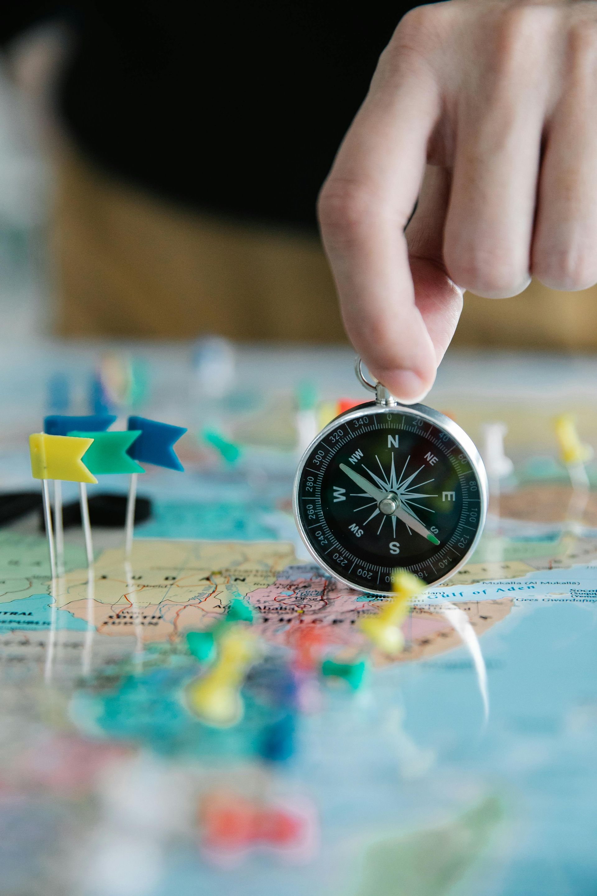 A person is holding a compass over a map with pins.