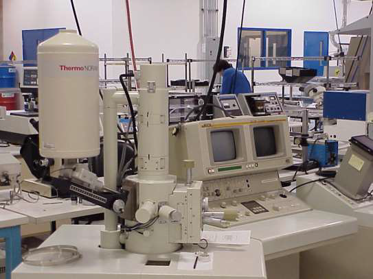 An industrial machine with a row of metal robotic arms placing small components onto a dark conveyor belt.