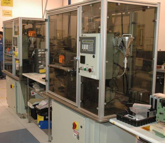 Two industrial automated machines housed in protective glass cabinets stand on a factory floor.