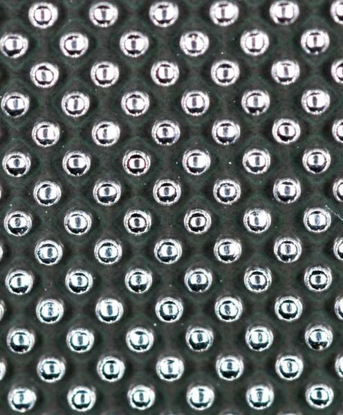 A close-up, top-down view of a dark, textured surface covered with a repeating pattern of small, metallic silver spheres.