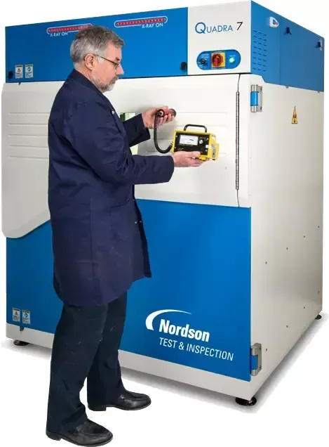 Man operating a Nordson Quadra 7 testing machine; blue and white color scheme.