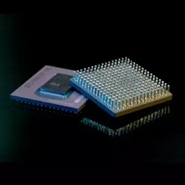 Two microprocessors, one with pins exposed, reflecting on a dark surface.