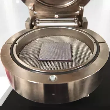 Open metal chamber with a square, purple object on a mesh screen.