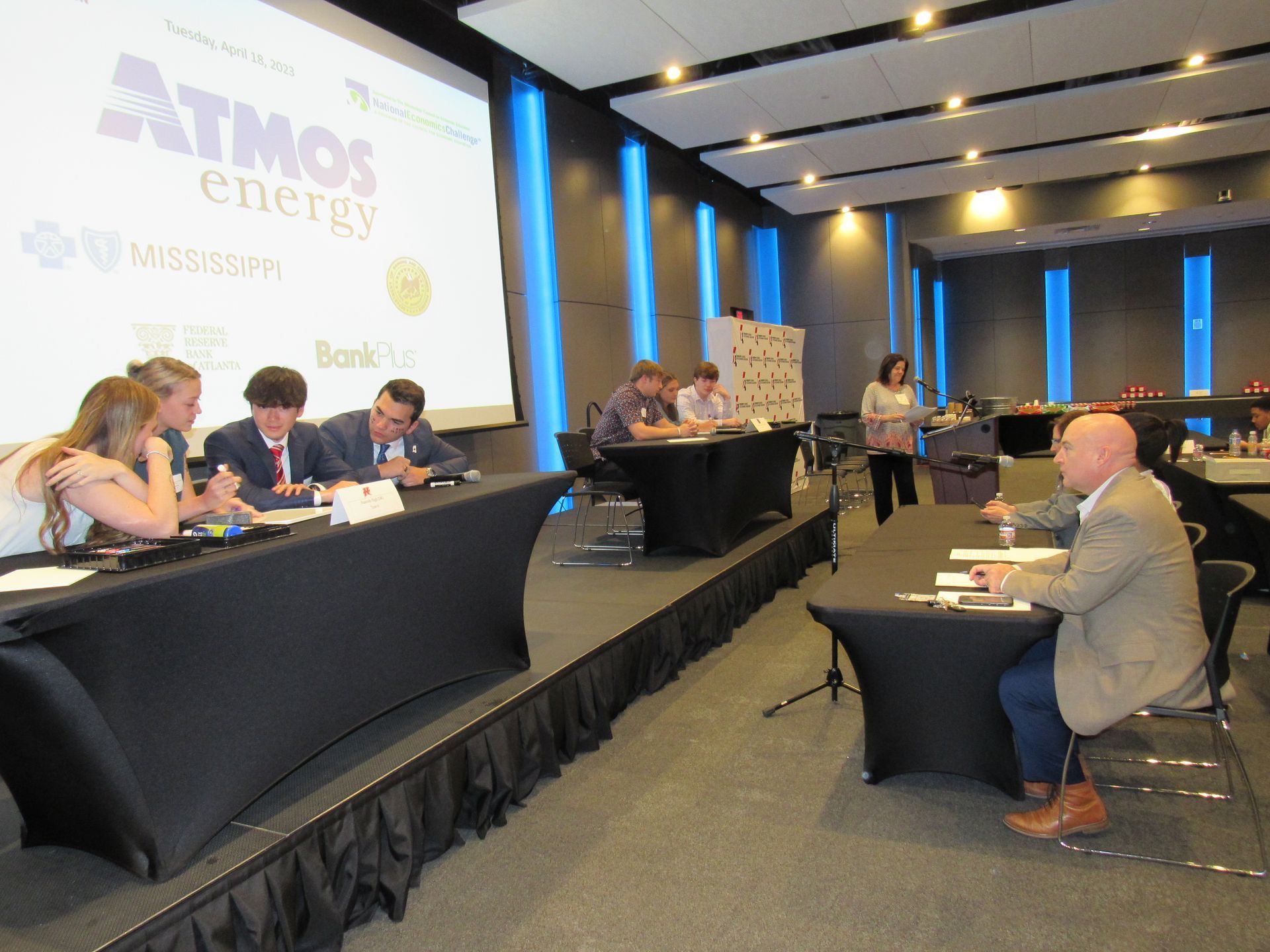 A group of people sitting at tables in front of a screen that says atmos energy