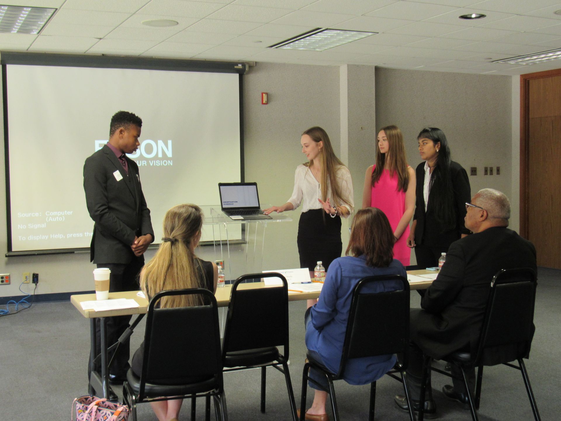 A group of people are sitting around a table in front of a projector screen that says ' on ' on it