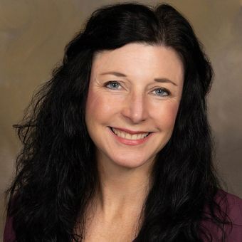 A woman with long black hair and blue eyes is smiling for the camera.