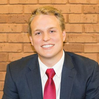 A man in a suit and tie is smiling in front of a brick wall