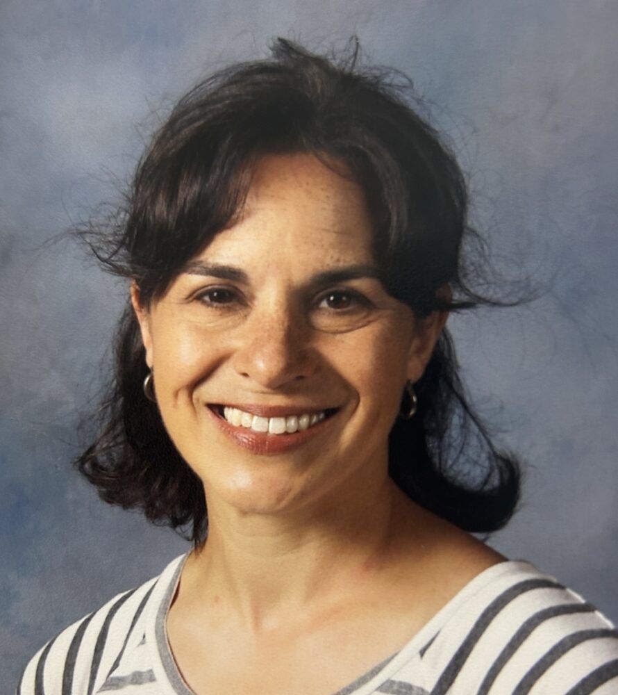 A woman in a suit and blue shirt is smiling for the camera.