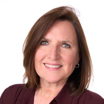 A woman with brown hair and blue eyes is smiling for the camera.