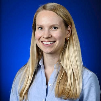 Smiling woman with long blonde hair in a light blue shirt against a blue background