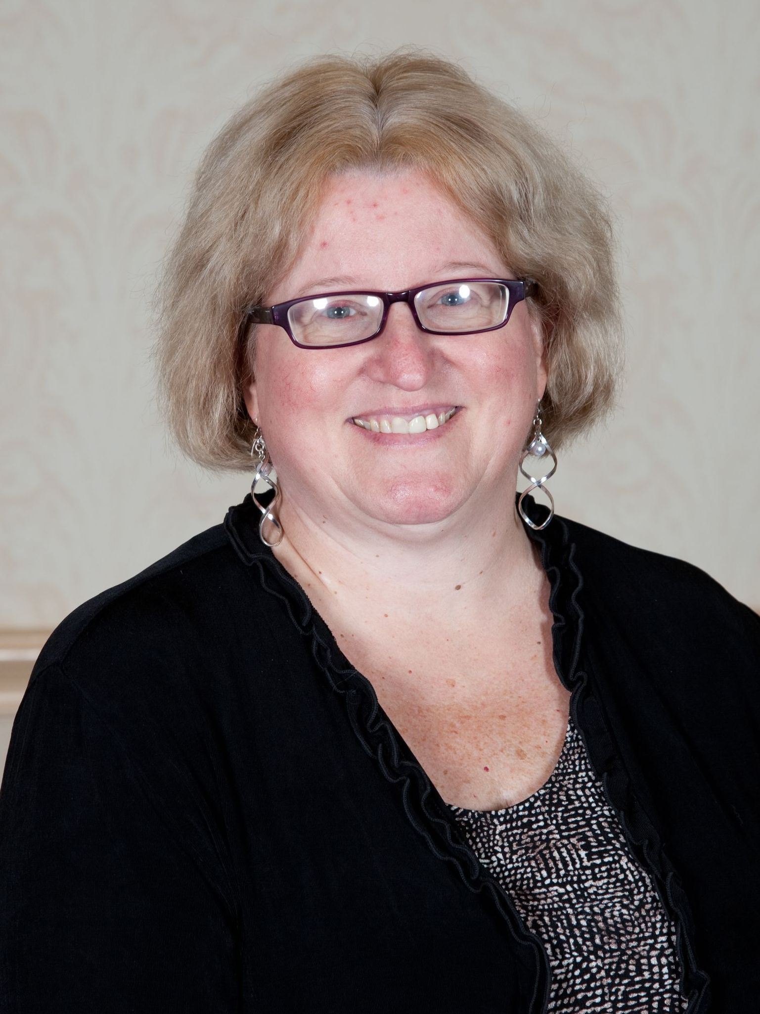 A woman wearing glasses and a black sweater smiles for the camera