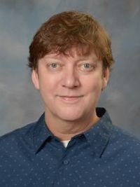 A man in a blue shirt is smiling for the camera.