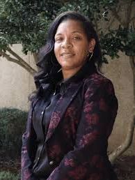 A woman in a purple jacket and black shirt is standing in front of a tree.