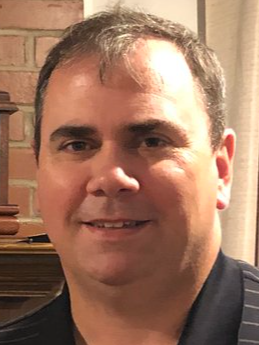 A close up of a man 's face with a brick wall in the background.