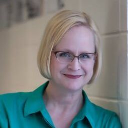 A woman wearing glasses and a green shirt is smiling for the camera.