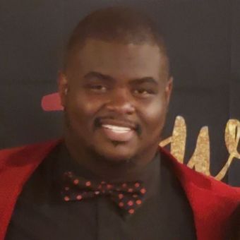 A man in a red suit and bow tie is smiling.