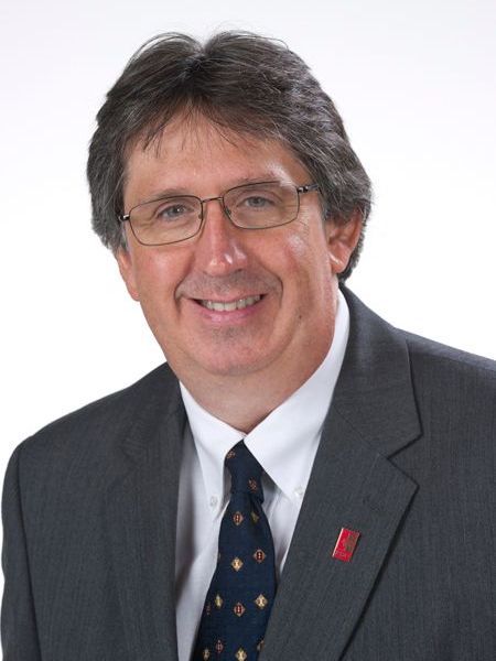 A man in a suit and tie with a red badge on his jacket