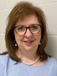 A woman wearing glasses and a pearl necklace is smiling for the camera.