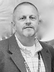 A black and white photo of a man in a suit and plaid shirt.