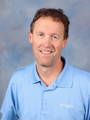 A man wearing a blue columbia polo shirt is smiling for the camera.