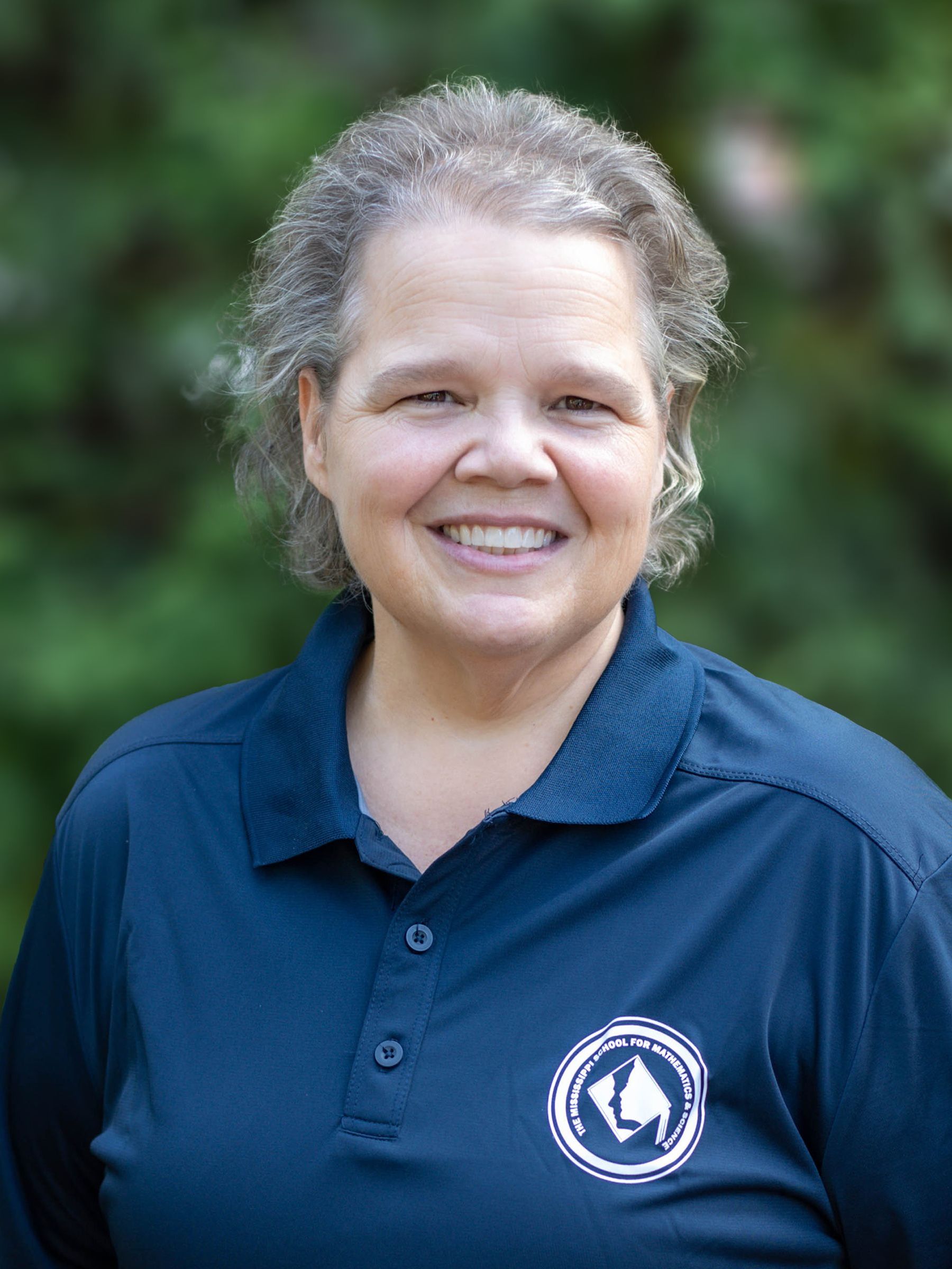 A woman wearing a blue polo shirt is smiling for the camera.
