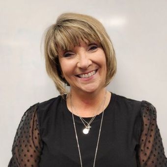 A woman wearing a black shirt and a necklace smiles for the camera