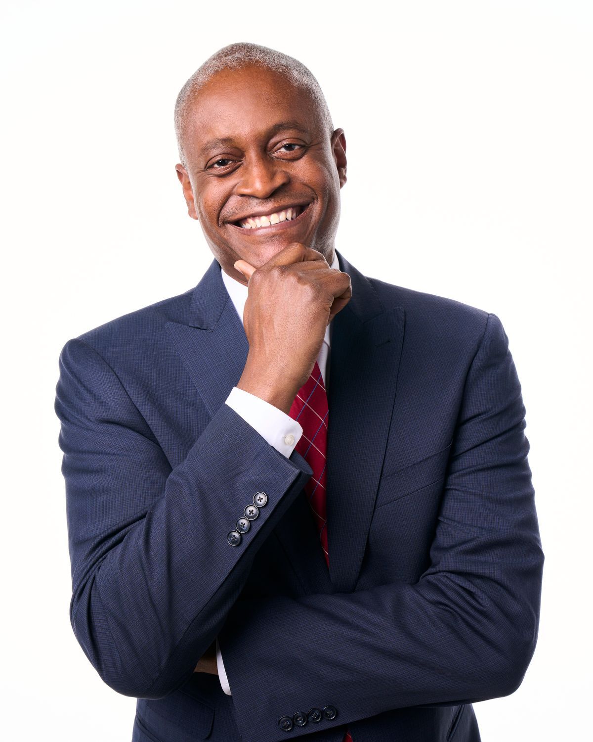 A man in a suit and tie is smiling with his hand on his chin