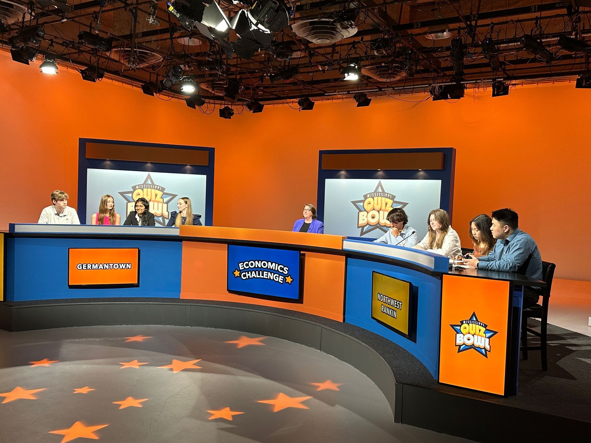 A group of people are sitting at a table in a studio with a sign that says 