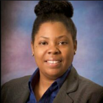 A woman in a suit and blue shirt is smiling for the camera.