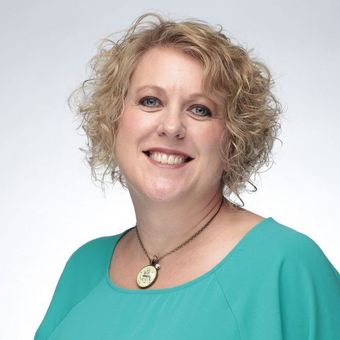 A woman wearing a blue shirt and a necklace smiles for the camera