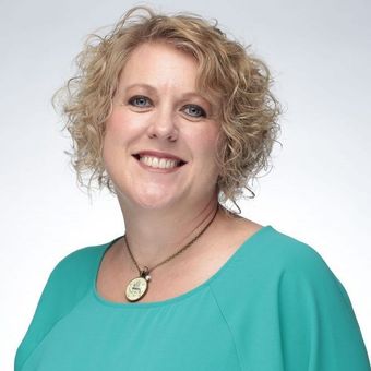 A woman wearing a blue shirt and a necklace smiles for the camera