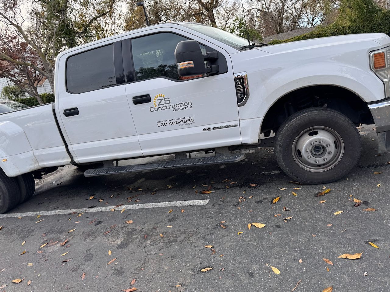 A white truck is parked on the side of the road in a parking lot.
