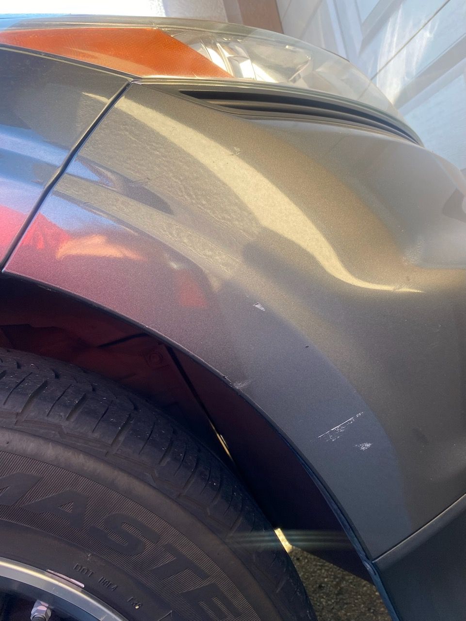 Close-up of a metallic grey car fender showing minor white surface scratches above the tire wheel arch.