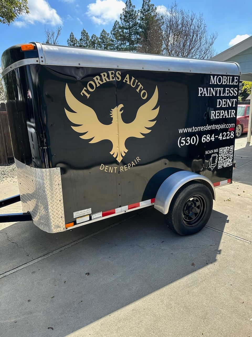 A black trailer with a bird on it is parked on the side of the road.