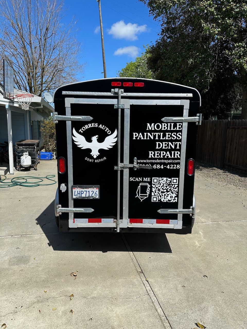 A mobile paintless dent repair trailer is parked in a driveway
