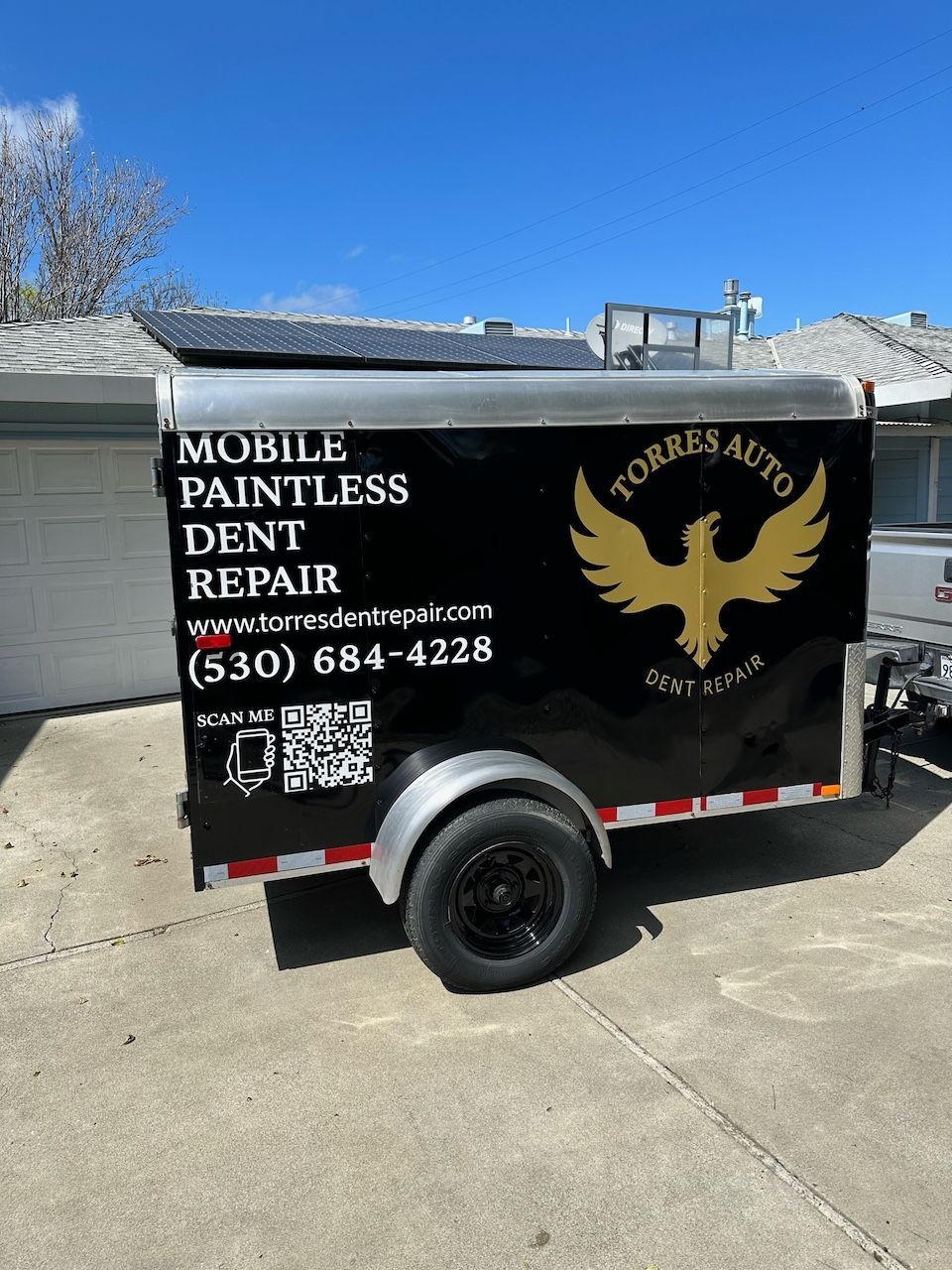 A mobile paintless dent repair trailer is parked in front of a house.