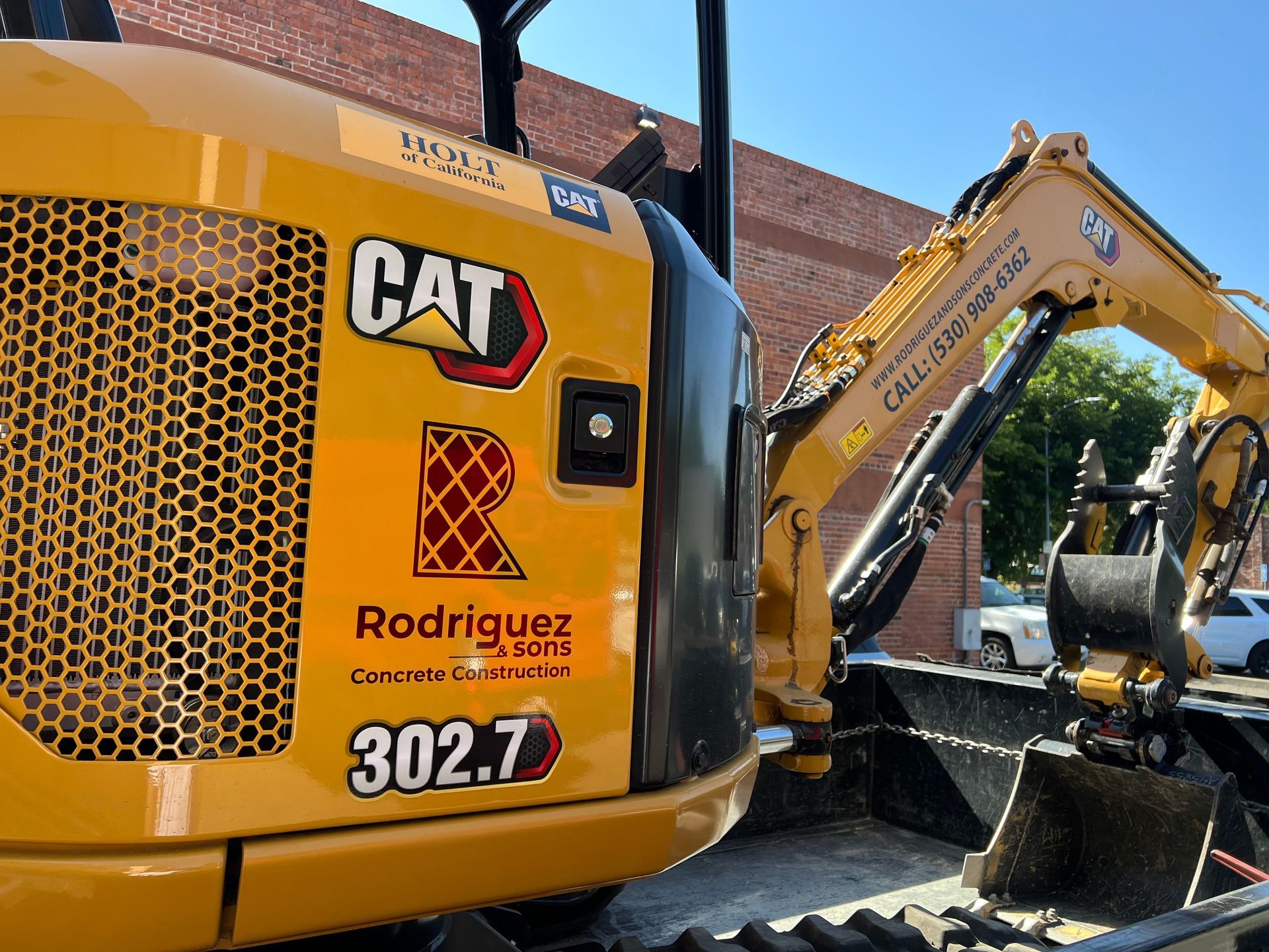 A yellow cat excavator is parked in front of a brick building