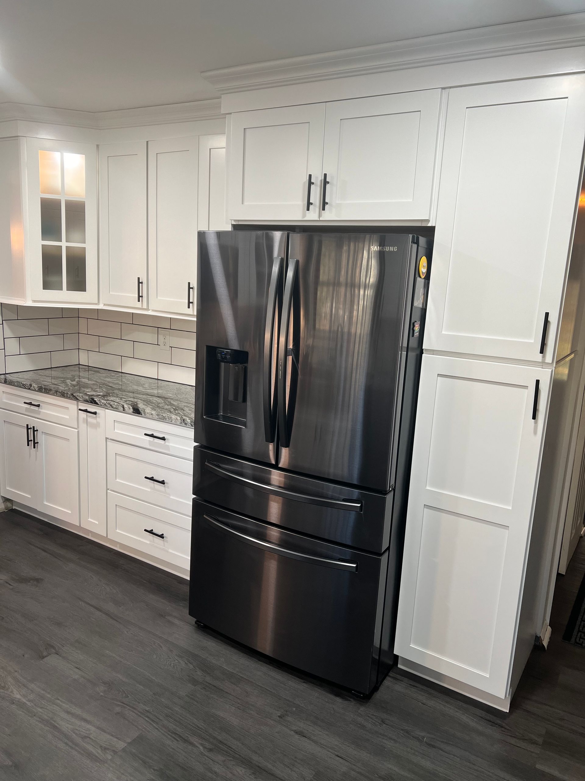 Black stainless steel refrigerator in a white kitchen with dark gray flooring.