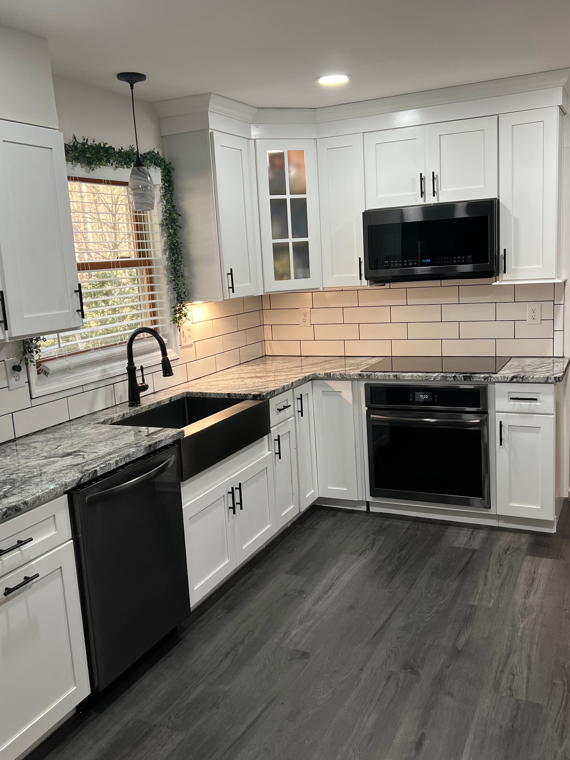 A modern kitchen featuring white cabinets, granite countertops, a black farmhouse sink, and dark stainless appliances.